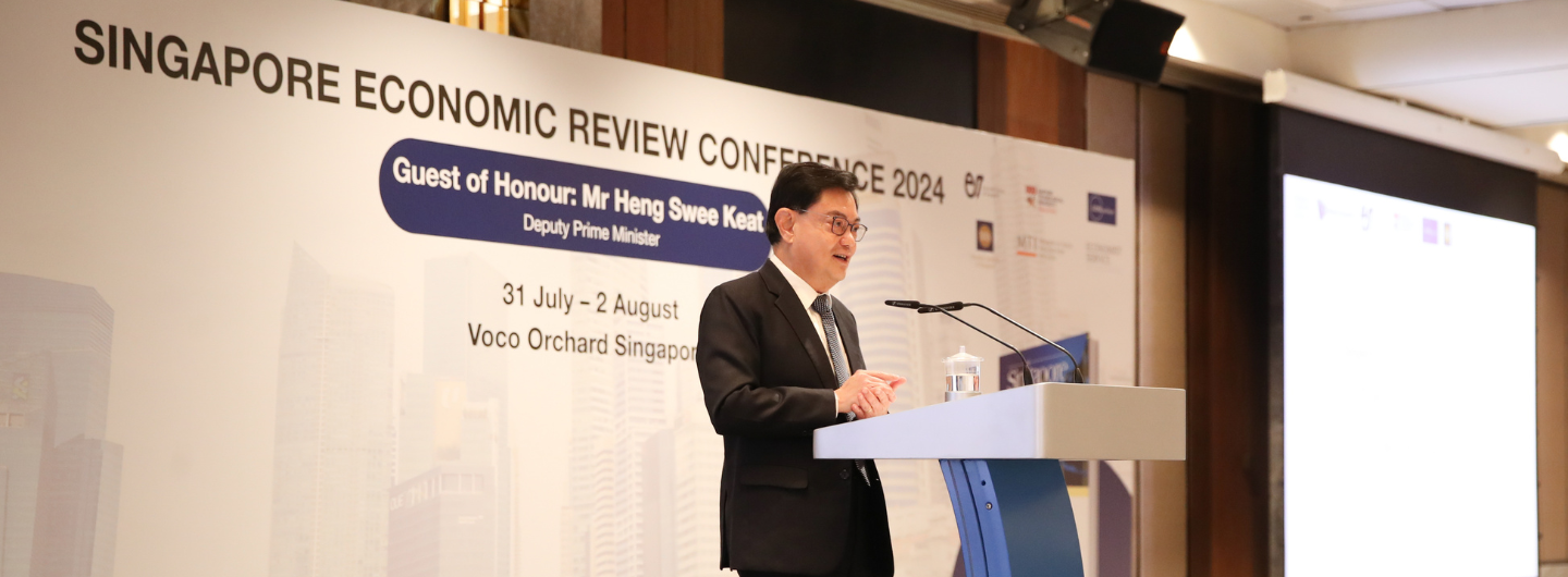 Man in suit speaking at podium at Singapore Economic Review Conference.